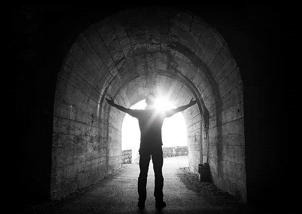 Ein Mann steht in einem dunklen Raum vor einem Tor durch das helles Licht einfällt