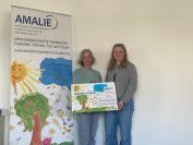 Plakat Kinderhospiz Amalie, Foto von Elena Fuchs u. Vertreterin d. Hospizes mit Spendenscheck.